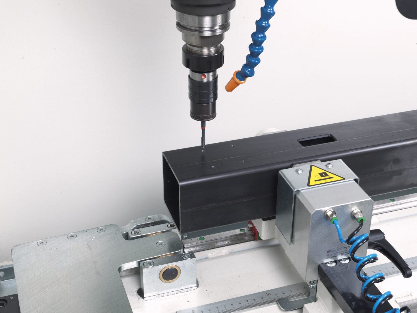 Rumba CNC machining center performing a precise drilling operation on a steel profile, secured by pneumatic clamps for stability.